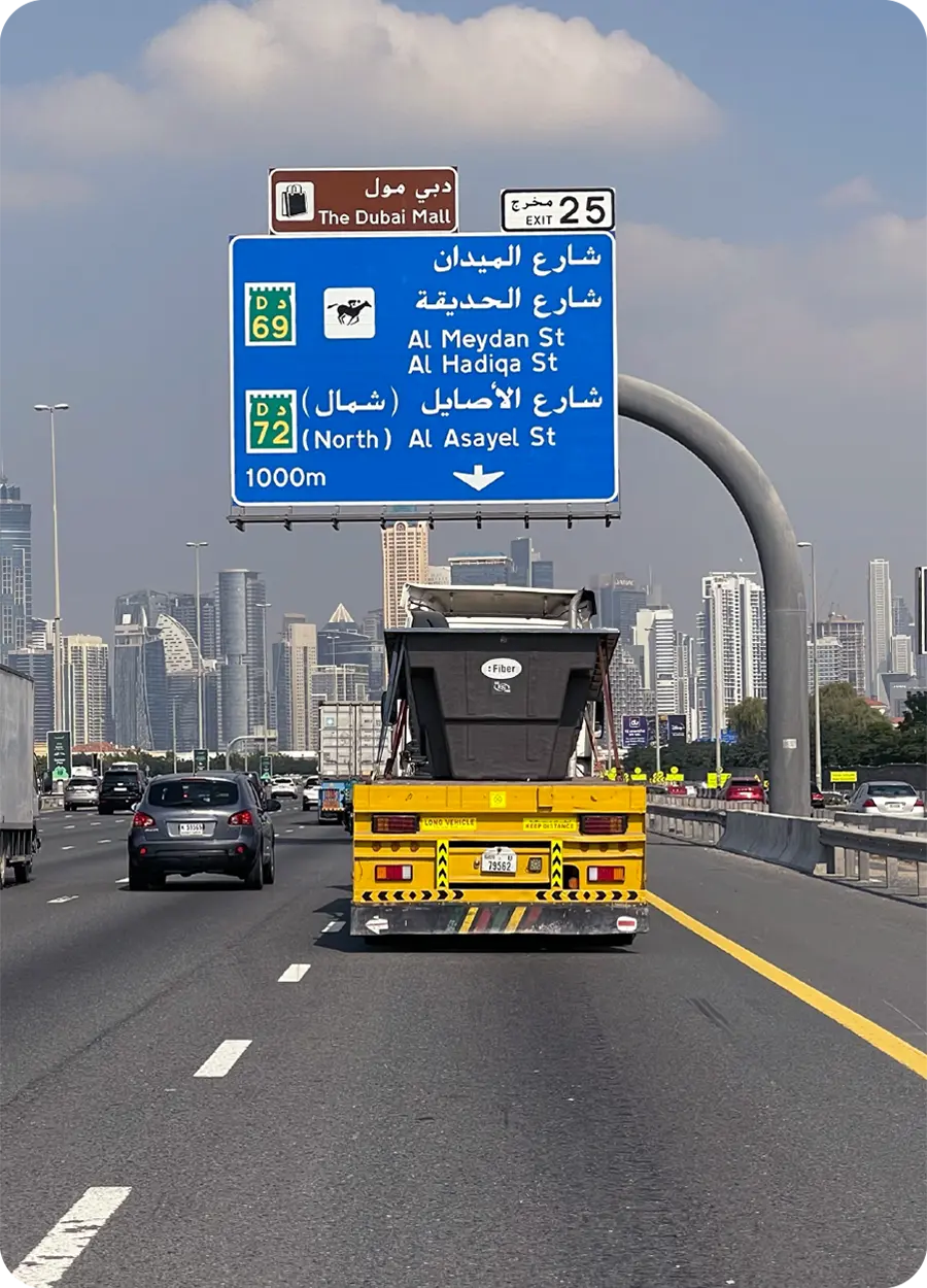 Rodovia em Dubai com placa em árabe e skyline ao fundo, representando a expansão internacional da Fiber